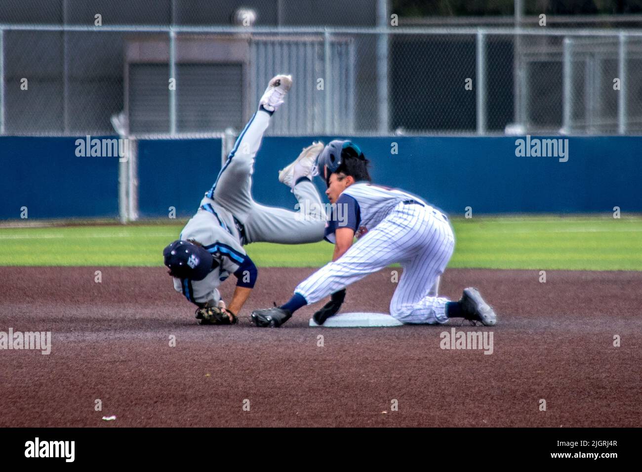 Ein College-Baseballspieler rutscht beim Versuch, zu stehlen, in die zweite Basis, während der zweite Basisspieler den Ball in seinem Baseballhandschuh hält, während er sich überrollt Stockfoto