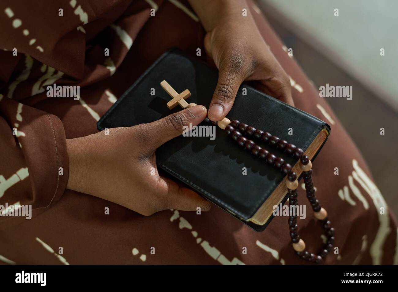 Hände von jungen afroamerikanischen Gemeindemitgliedern der katholischen oder evangelischen Kirche, die Bibel und Rosenkranz während der Predigt oder des Gebets halten Stockfoto