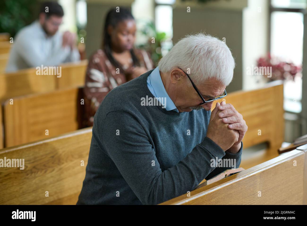 Reifer Mann neigt seinen Kopf und beugt sich über seine Hände zusammen während stillem Gebet nach Predigt oder vor Kommunion in der Kirche Stockfoto