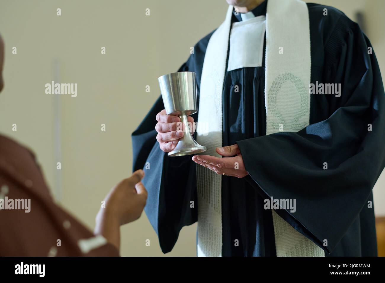 Geistlicher der katholischen Kirche hält einen Becher mit Wein zum Opferritus, während er vor einer afroamerikanischen Pfarrerin steht Stockfoto