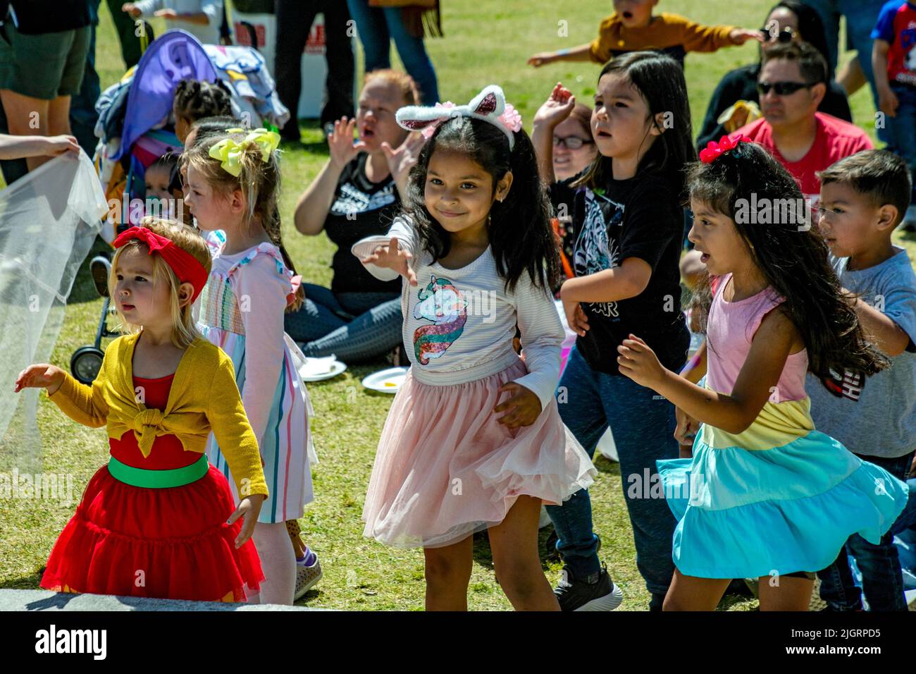 Fröhliche, multirassische Kinder singen und tanzen zu einer Unterhaltung im Freien, die in einem Park in Costa Mesa, CA, stattfindet. Stockfoto