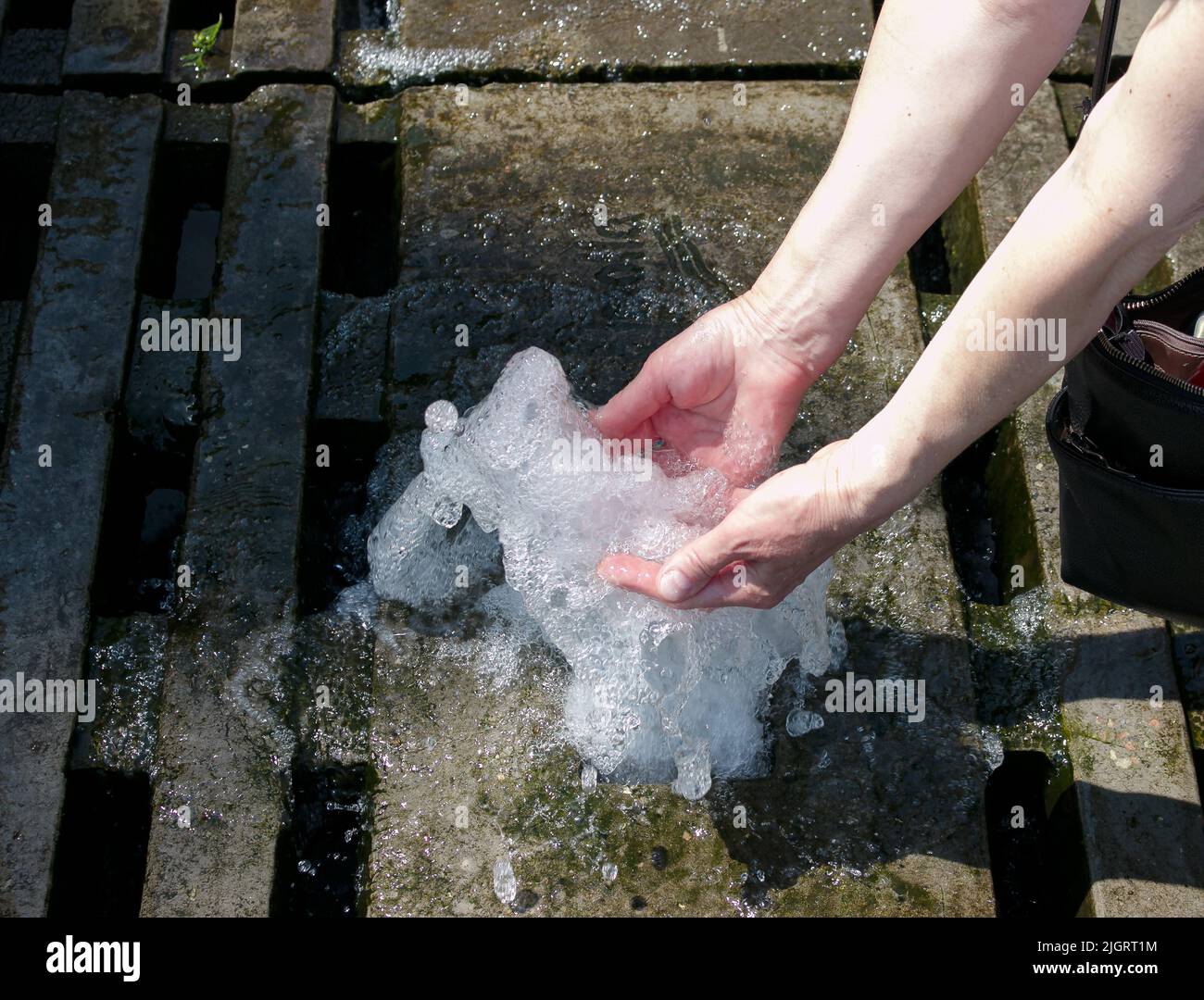 Hände berühren den Brunnen. Ein Wasserstrom aus dem Brunnen wird von Händen berührt. Frische und Kühle Konzept Stockfoto