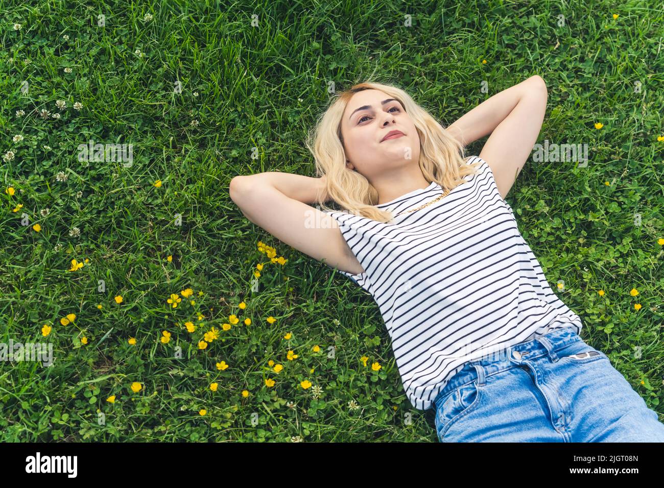 Ruhiges, friedliches, junges blondes Mädchen, das auf dem Gras liegt und die Hände unter dem Kopf hält und träumt. Mittlerer Schuss. Hochwertige Fotos Stockfoto