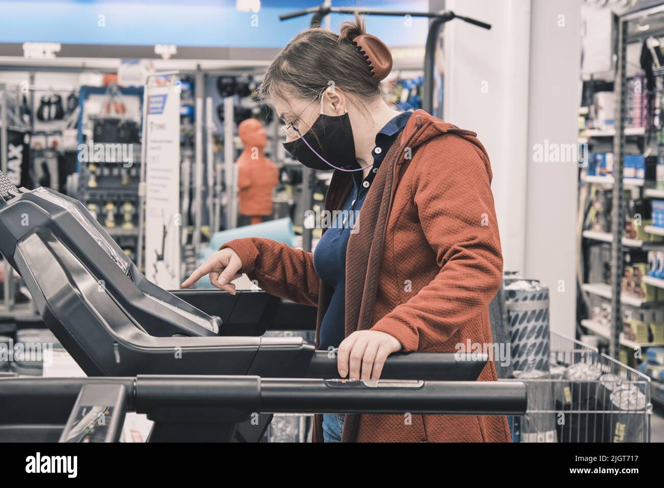 Eine Frau mit Brille und Maske gegen Viren kauft in einem Geschäft ein großes Laufband Stockfoto