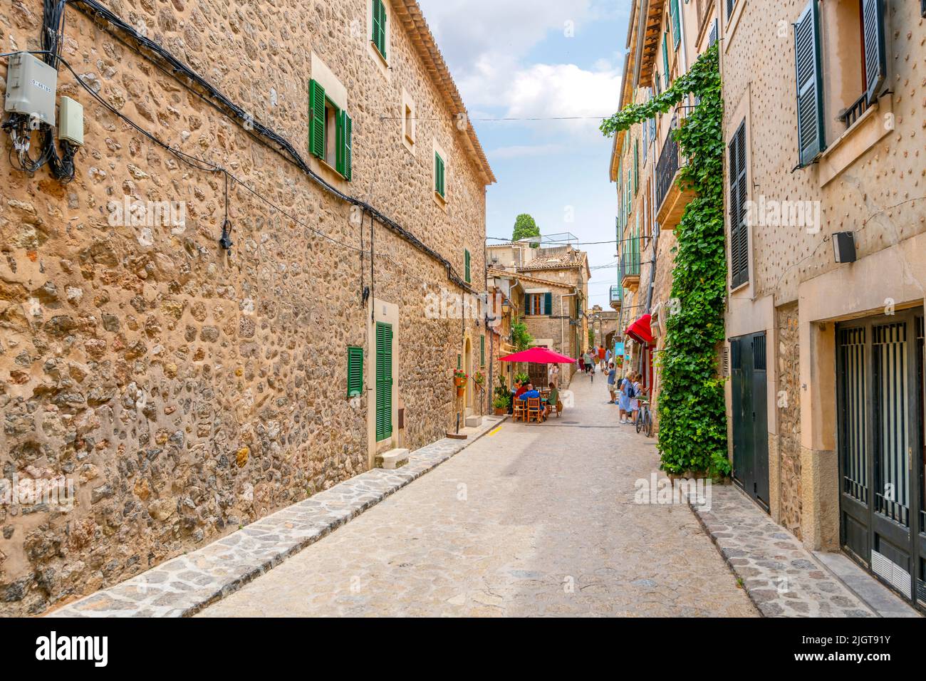 Eine der vielen malerischen, von Bäumen gesäumten Straßen mit Geschäften und Cafés im Dorf Valldemossa, Spanien, auf der Insel Mallorca, Spanien. Stockfoto