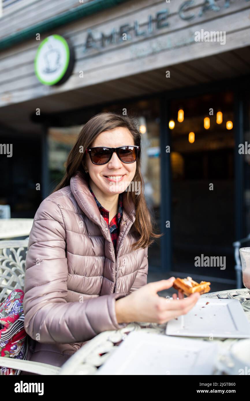 Eine Frau in einem Café, die Waffeln zum Nachtisch isst. Vertikales Foto. Stockfoto