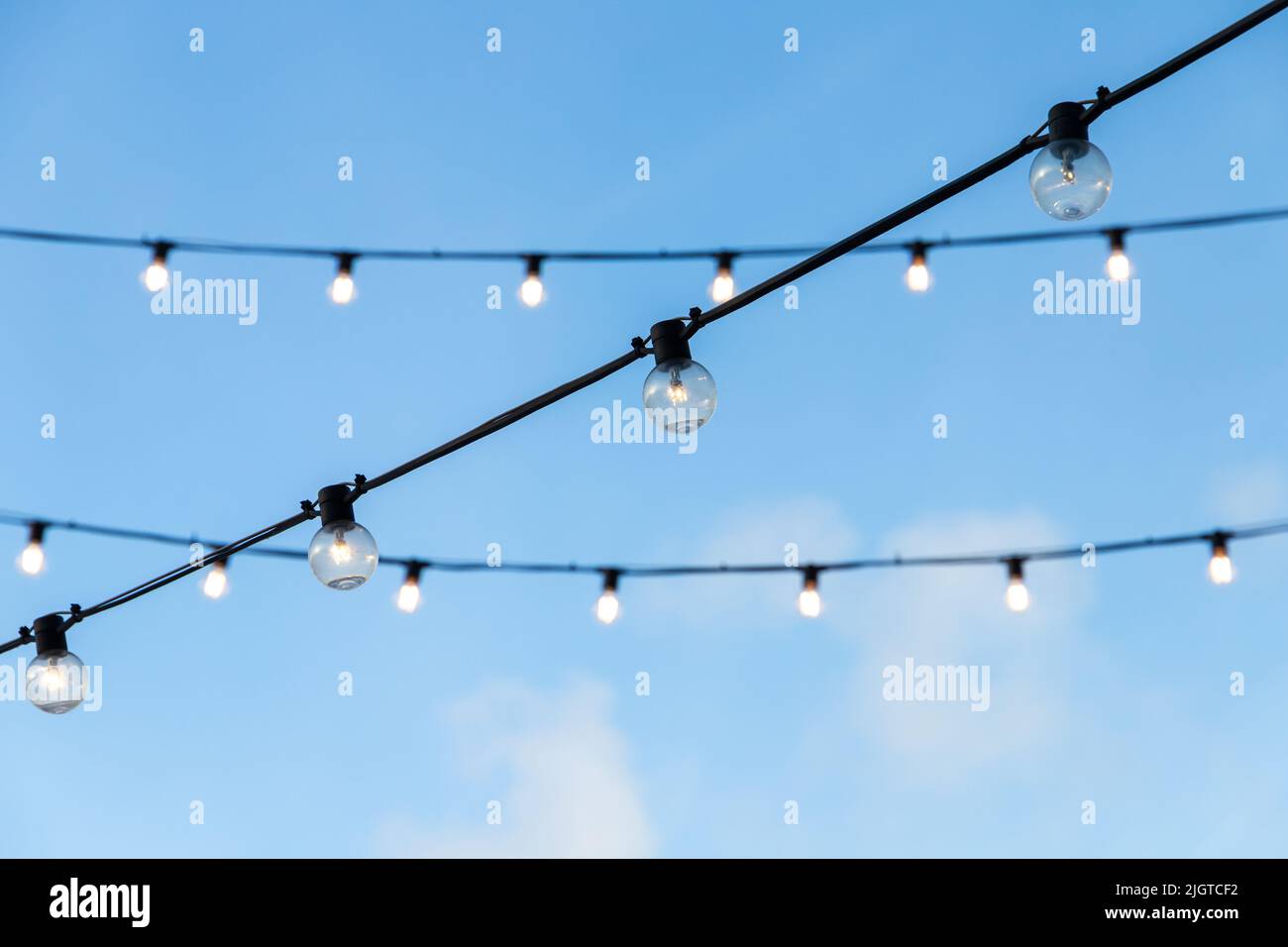 Unter blauem Abendhimmel hängen Strassenskränze aus Glühbirnen, die an schwarzen Drähten hängen Stockfoto