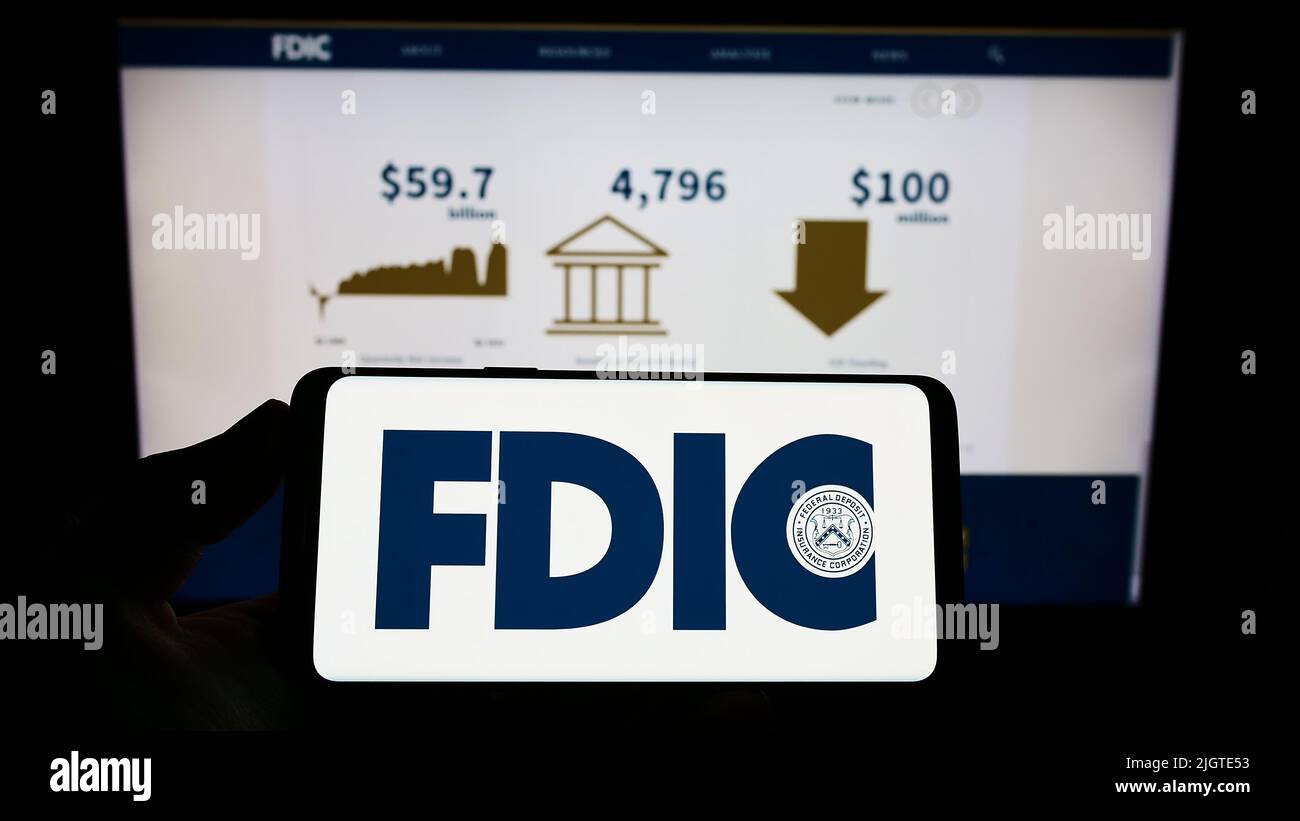 Person, die das Smartphone mit dem Logo der US Federal Deposit Insurance Corporation (FDIC) auf dem Bildschirm vor der Website hält. Konzentrieren Sie sich auf die Telefonanzeige. Stockfoto