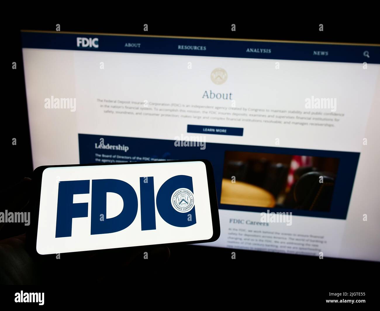 Person mit Mobiltelefon und Logo der US Federal Deposit Insurance Corporation (FDIC) auf dem Bildschirm vor der Webseite. Konzentrieren Sie sich auf die Telefonanzeige. Stockfoto