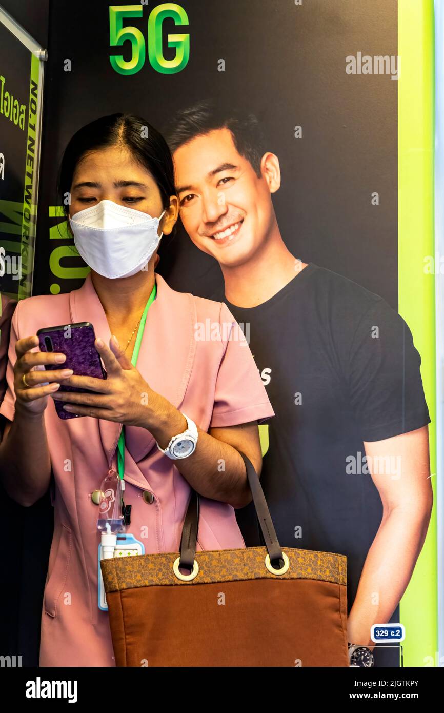 Thailändischer Passagier mit Gesichtsmask, der vor dem Werbespot im BTS Skytrain, Bangkok, Thailand, telefoniert Stockfoto