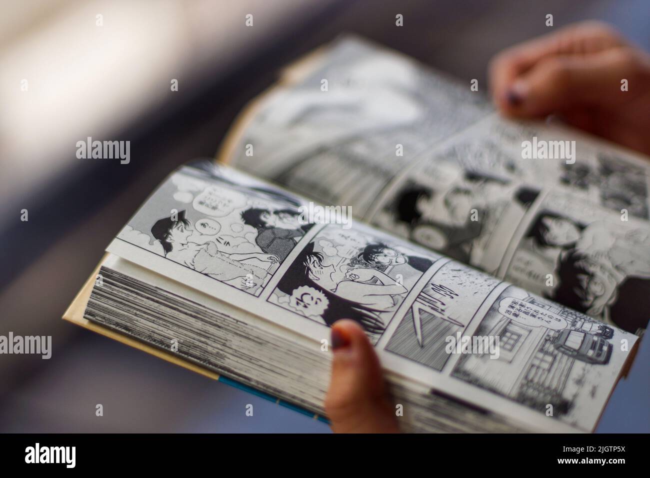 Nahaufnahme einer erwachsenen Person Hände öffnen und halten ein japanisches Comic-Buch mit Bokeh Hintergrund. Stockfoto