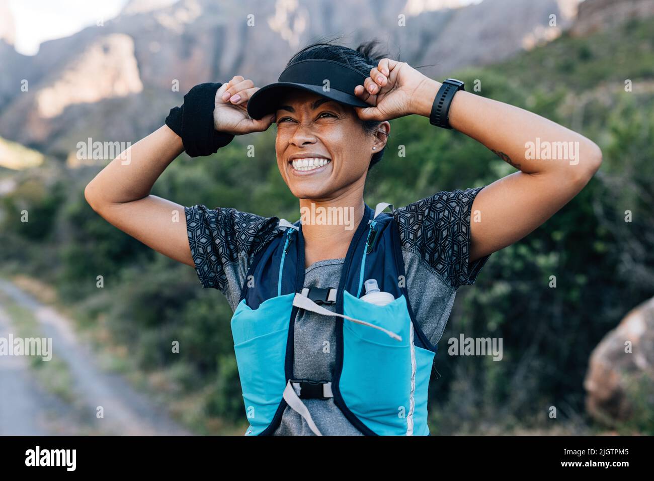 Lachende Frau, die Mütze hält und die Aussicht genießt. Junge Frau im Sport tragen in wildem Gelände. Stockfoto