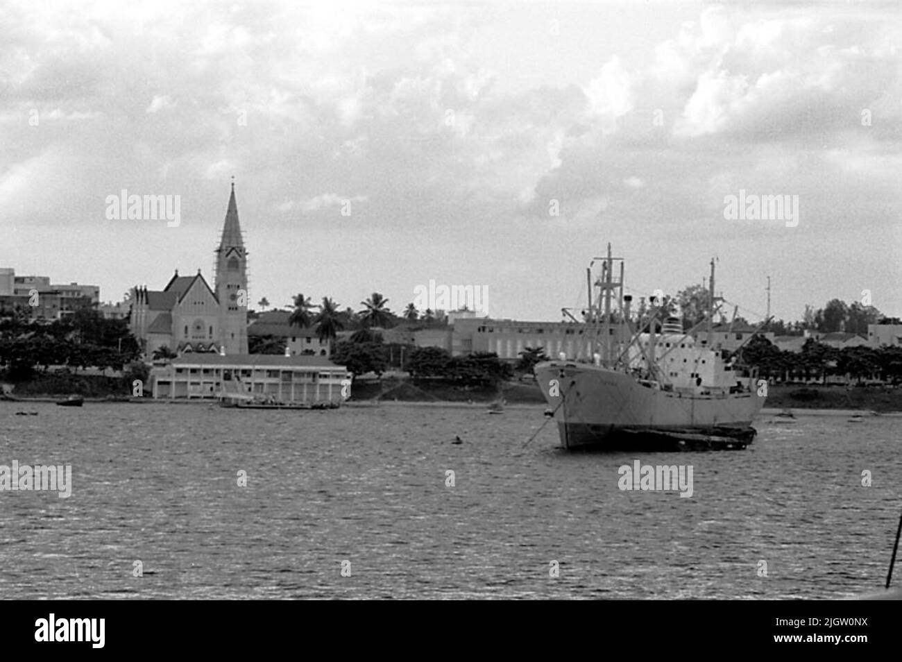 Ein größeres Frachtschiff befindet sich in einer Meeresbucht. In der Bucht ist eine Gesellschaft. Links ist eine Kirche. African travel36 Bilder in Serie. Stockfoto