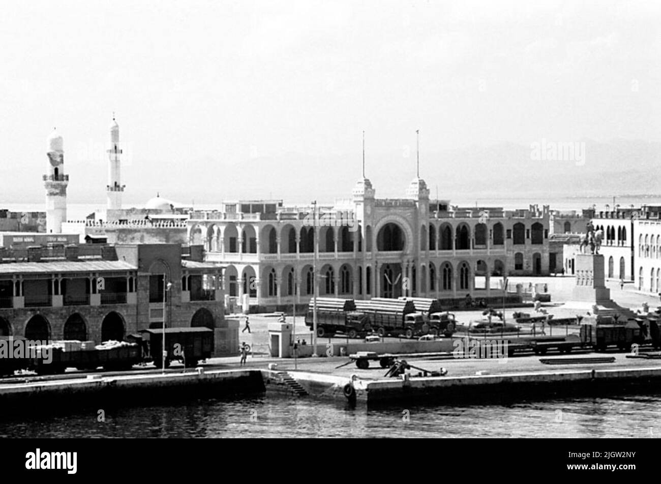 Das Foto wurde ungefähr 1961-08-30 aufgenommen. Ein Hafen in einer Gemeinschaft. Sie sehen ein großes Gebäude, das ein Rathaus mit zugehörigen Plätzen sein kann. Auf dem Platz befindet sich eine große Statue. Auf dem Platz stehen auch drei Lastwagen. Entlang des Hafens gibt es Eisenbahnwaggons. Auf der linken Seite sind zwei Minarette (oder Aussichtsturm). African travel35 Bilder in Serie. Stockfoto