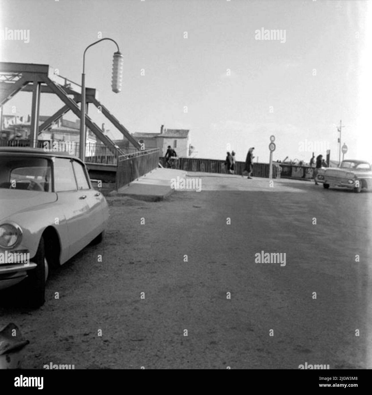 30. Frankreich. Fotojournal ist bei B.M.A. erhältlich + Fotoalben. Erwerb: Bücher und Archivmaterial. Fotos aufgenommen 1959-11-06,12 Bilder in Serie. Nach Angaben: Frankreich. Die Mittelmeerküste, Martigues, 6/11-59. Der Eingang zur Brücke. Eine Brücke geht über eine Wasserbewegung in einer Gemeinde. Im Vordergrund stehen zwei Autos, die geparkt sind. Ein Mann radelt auf der Brücke. Mehrere Frauen gehen an der Brückenhalterung. Stockfoto