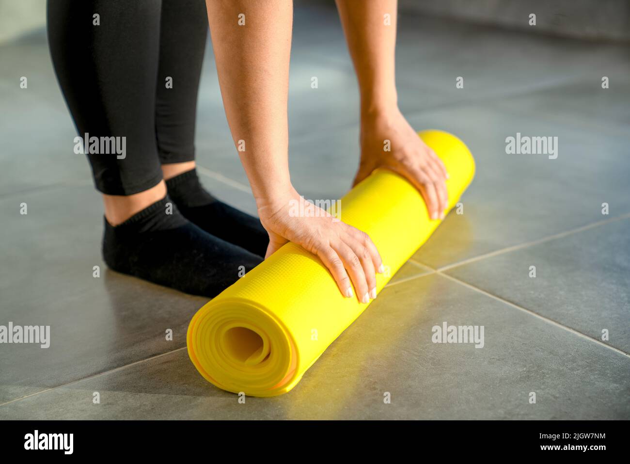 Frau bereitet sich darauf vor, die gelbe Rolle der Sportmatte für die Fitness auszupacken. Die Hände liegen aus nächster Nähe auf der Matte. Konzept eines gesunden Lebensstils. Stockfoto