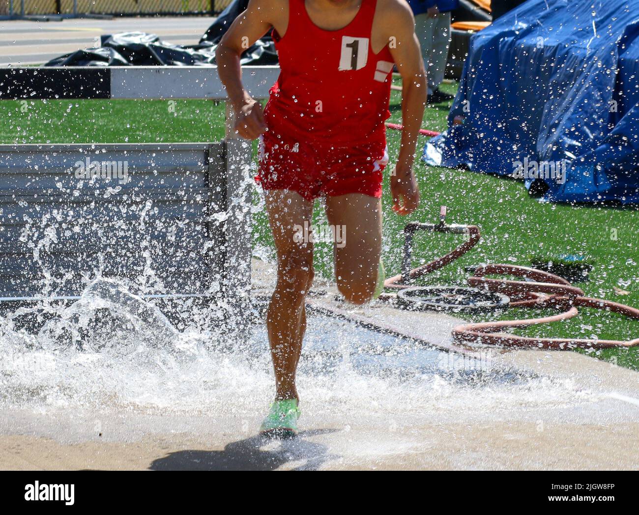 Ein High-School-Junge in einer roten Uniform, der während eines Rennens im Wasser des Hindernisrennens planscht. Stockfoto