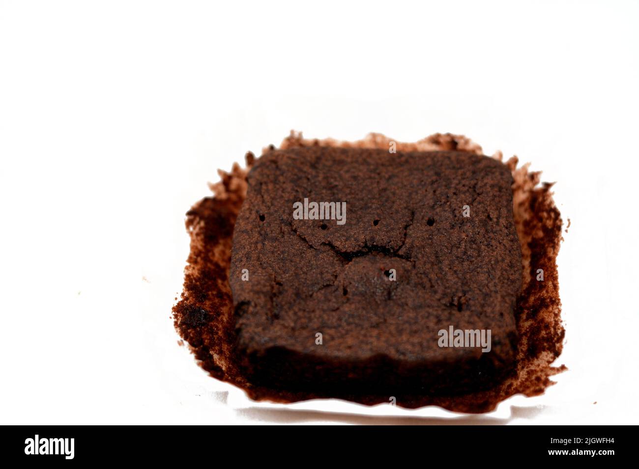 Süßes Brownie-Schokoladenkuchenstück isoliert auf weißem Hintergrund, selektiver Fokus von Brownie-Scheibe mit Kakaopulver auf einem üblichen Butterpapier Stockfoto
