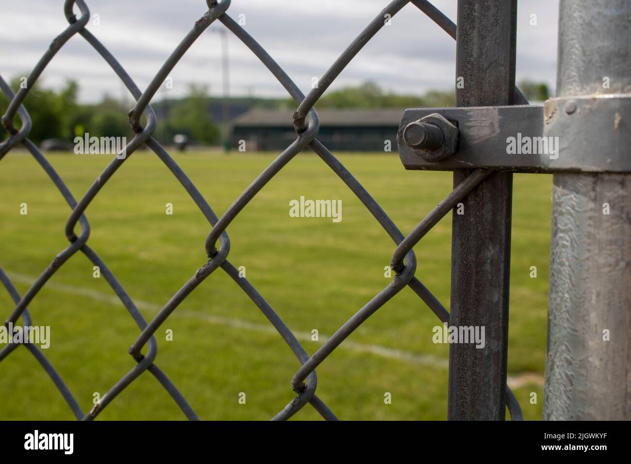 Blick durch einen galvanisierten Kettenglied Zaun Baseballgras und Bäume in der Ferne Stockfoto