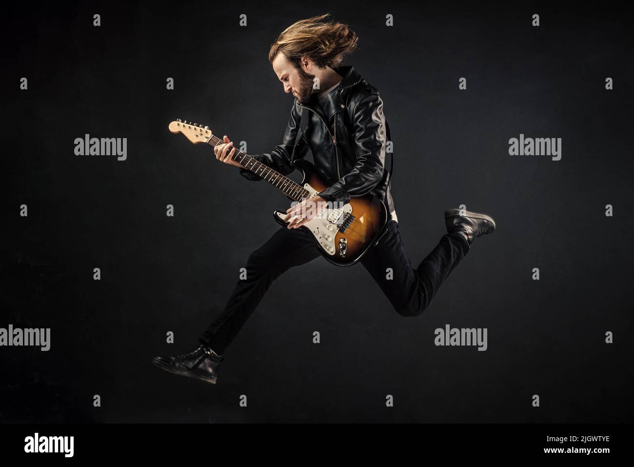 Emotionaler bärtiger Rockmusiker, der E-Gitarre in Lederjacke spielt und hüpft, Basgitarre Stockfoto