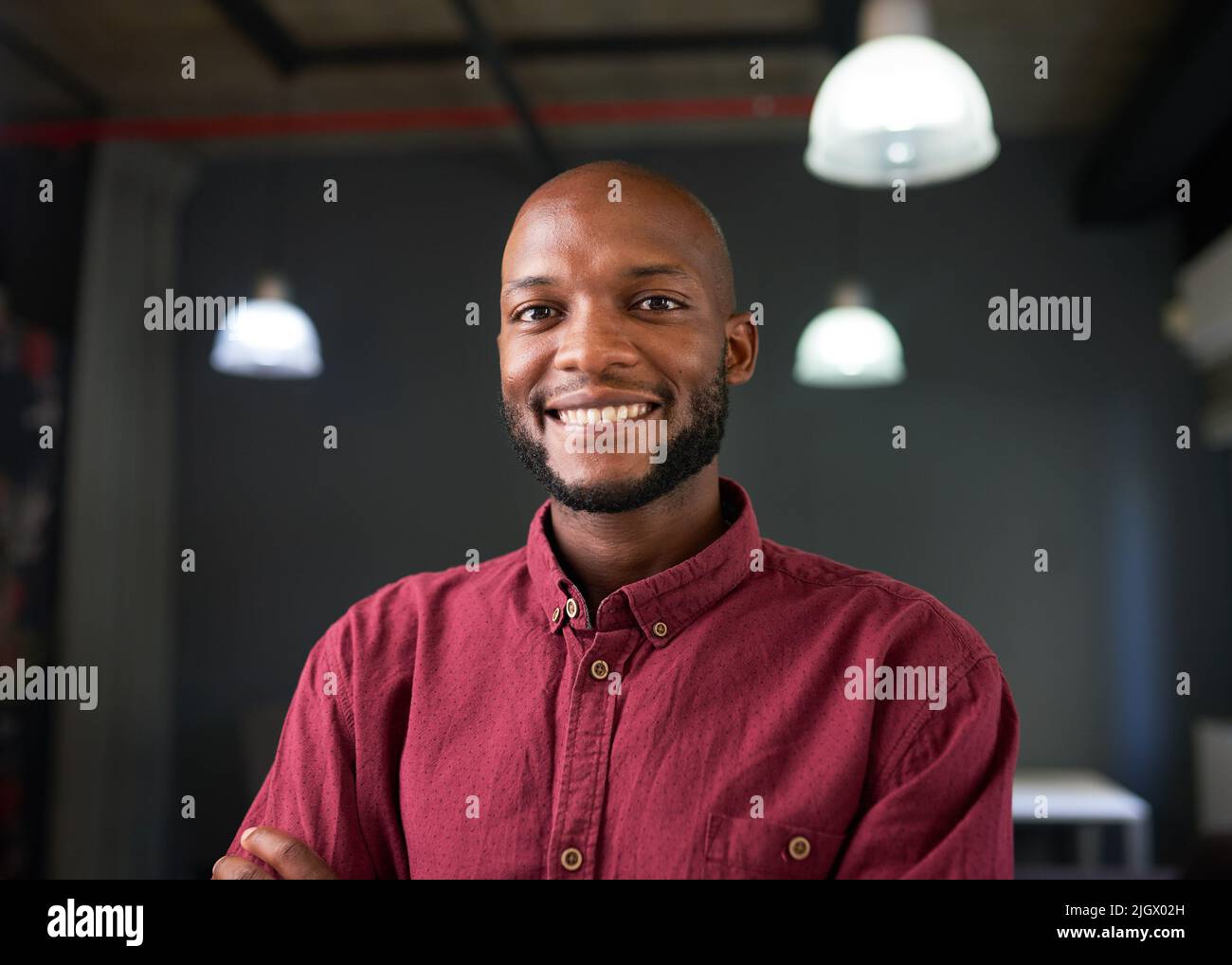 Ein selbstbewusster, glücklicher schwarzer Mann posiert in einem roten Hemd in einem Industriebüro Stockfoto