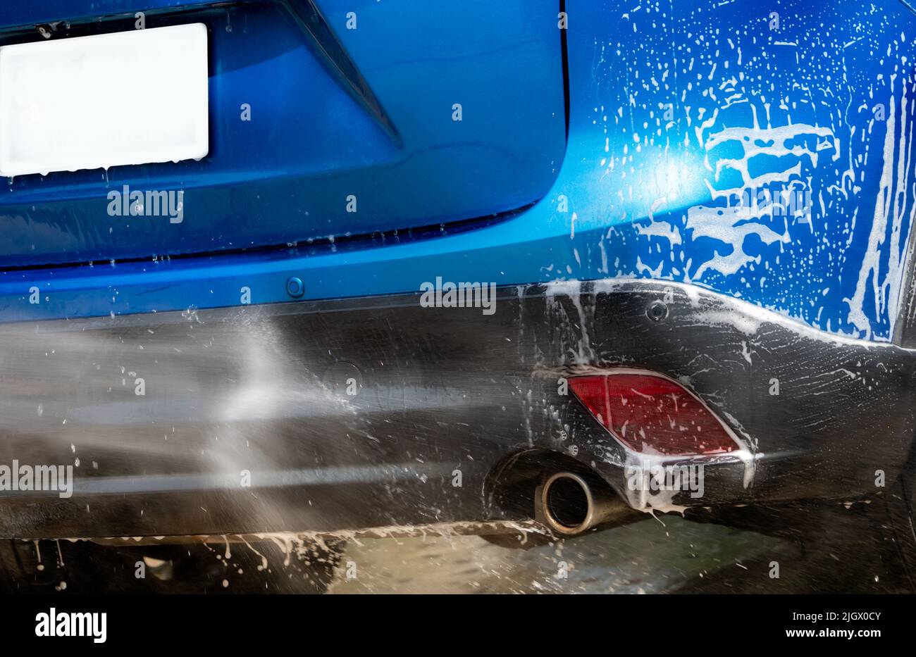 Autoreinigung mit Hochdruck-Wasserspray. Blaue Autowäsche mit weißem Seifenschaum. Kfz-Pflegebereich. Nahaufnahme Auto Reinigung und Glanz vor dem Wachsen Stockfoto