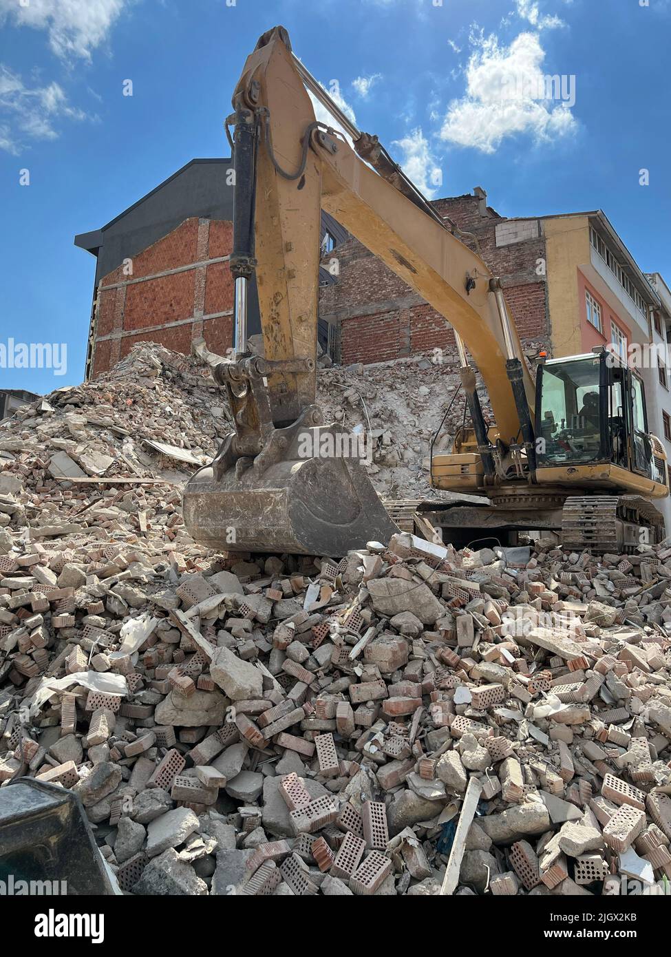 Gebäude oder Haus, das von einem gelben Bagger abgerissen wurde. Gefährliches Baugebiet. Baumaschine, die unter der heißen Sommersonne arbeitet. Stockfoto