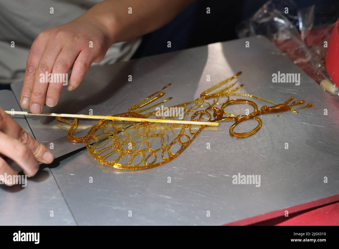 Zuckermalerei in China. Eine traditionelle chinesische Volkskunst mit heißem, flüssigem Zucker, um zweidimensionale Tiere auf einer Metalloberfläche zu kreieren. Stockfoto