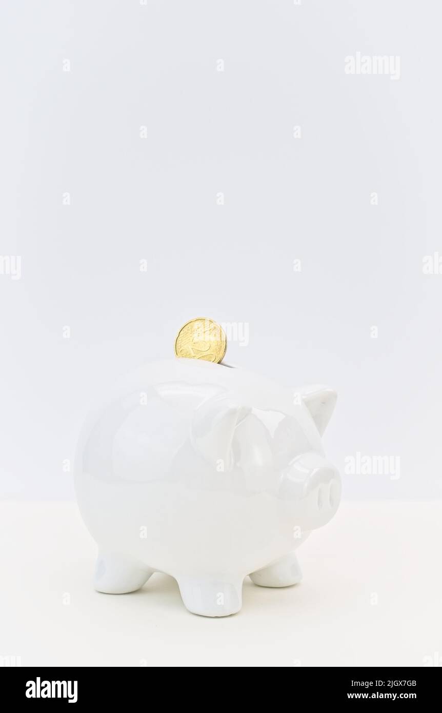 euro-Münze und weißes Sparschwein auf einem weißen Schreibtisch - Sparungs- und Inflationskonzepte Stockfoto