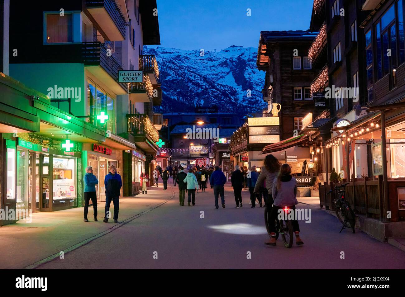 ZERMATT, SCHWEIZ - APR 11, 2022: Touristen gehen und besichtigen auf einer Straße in der Stadt Zermatt bei Sonnenuntergang. Stockfoto