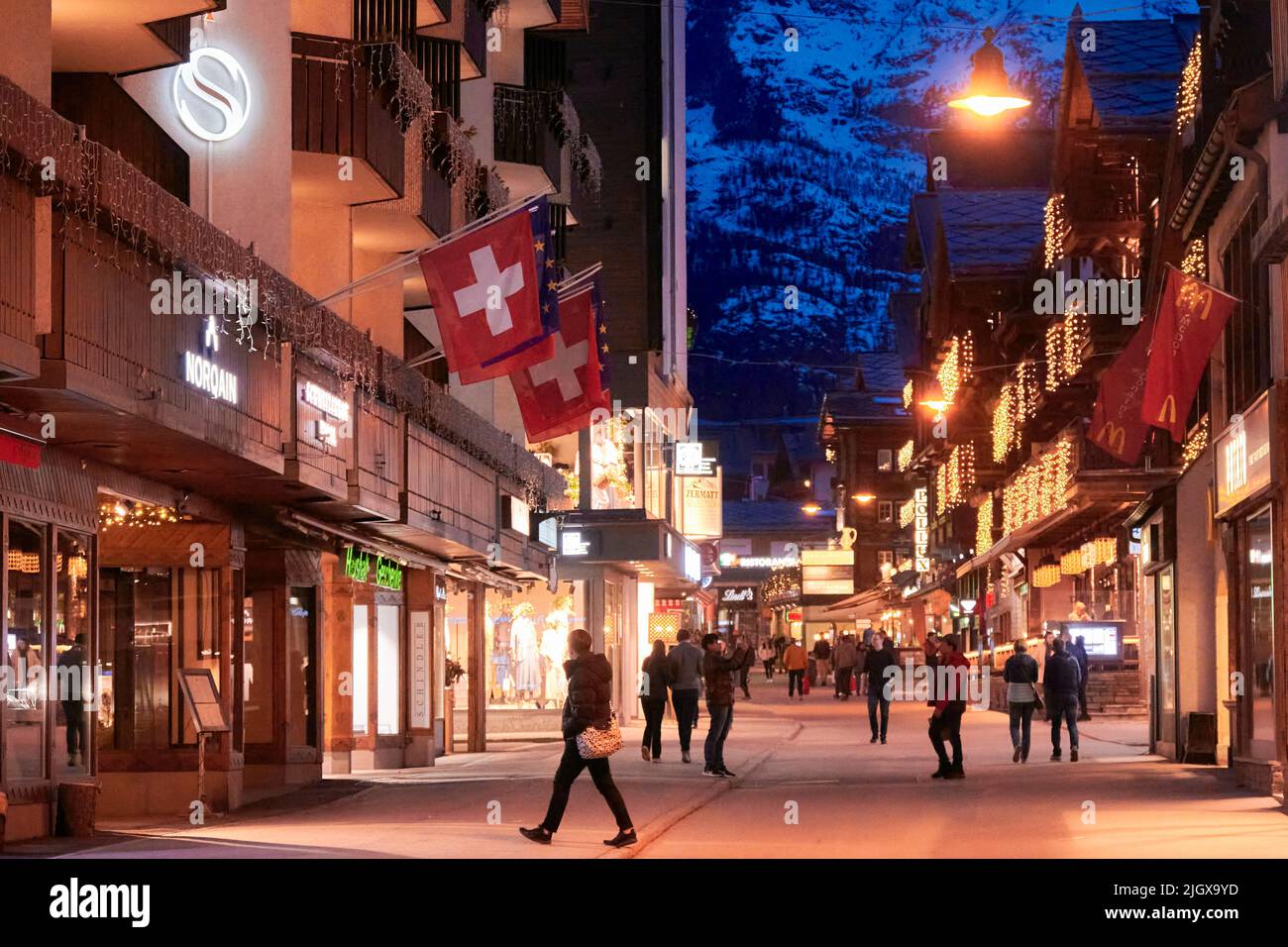 ZERMATT, SCHWEIZ - APR 11, 2022: Touristen gehen und besichtigen auf einer Straße in der Stadt Zermatt bei Sonnenuntergang. Stockfoto
