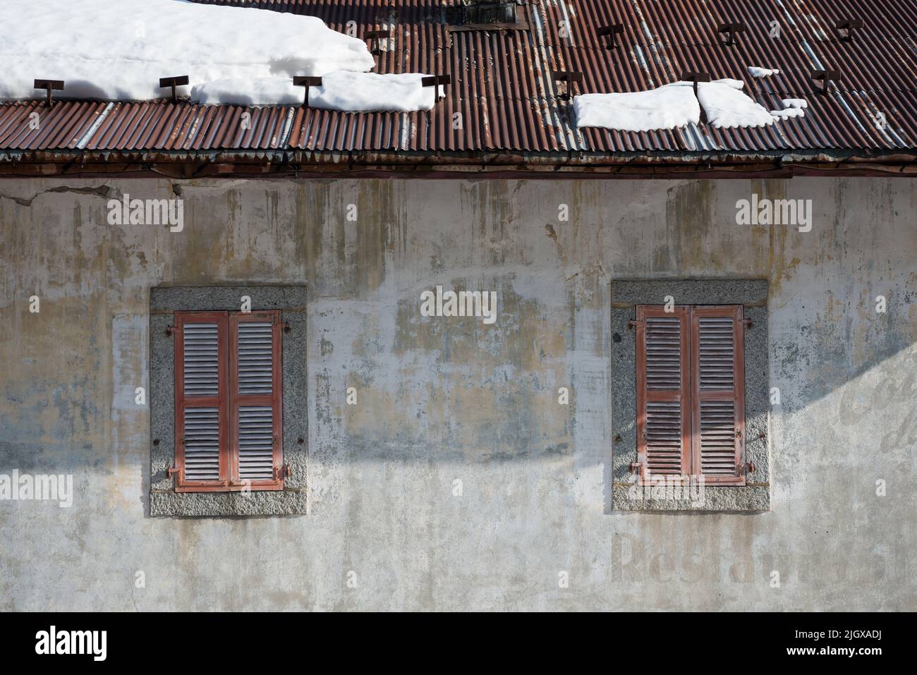 Verfallene, alternde Fassadenwand des klassischen französischen Alp-Chalet-Gebäudes mit roten Fensterläden und Wellblechdach mit Frühlingsschnee in Le Tour France Stockfoto