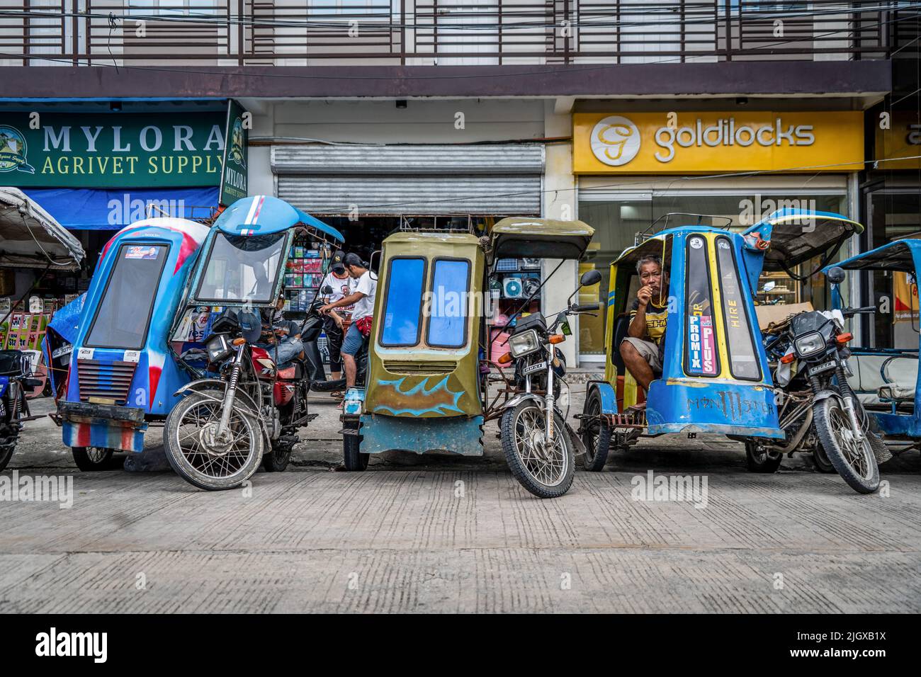 Moalboal, Philippinen. 13.. Juli 2022. Motorrad-Dreirad-Fahrer machen eine Pause, während sie vor einer belebten öffentlichen Bushaltestelle auf Kunden warten. Tägliches Leben im Moalboal District, Cebu, Philippinen. Das Gebiet, das einst für sein Tauchen und seine massiven Sardinenwolken bekannt war, hat sich schwer getan, den Tourismus wieder zu beleben, auch nachdem die Reisebeschränkungen von Covid-19 aufgehoben wurden, da die Infrastruktur durch den Taifun Rai, auch bekannt als Super Typhoon Odette, beschädigt wurde, was einen Großteil des Gebiets dezimiert und mit dem Wiederaufbau zu kämpfen hat. Kredit: SOPA Images Limited/Alamy Live Nachrichten Stockfoto