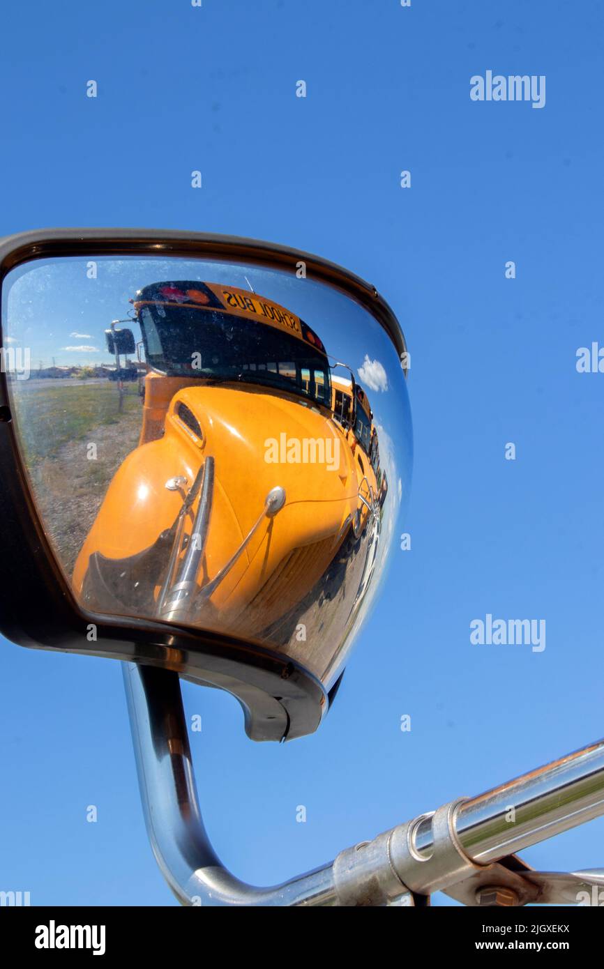 Ein großer, gelber Schulbus spiegelt sich im Seitenspiegel des davor fahrenden Busses wider und bringt ein modernes, abstraktes Gefühl in den öffentlichen Bildungsverkehr Stockfoto