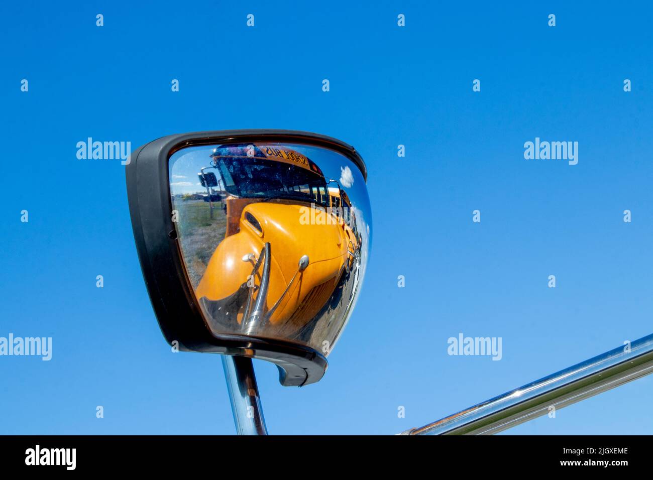 Ein großer, gelber Schulbus spiegelt sich im Seitenspiegel des davor fahrenden Busses wider und bringt ein modernes, abstraktes Gefühl in den öffentlichen Bildungsverkehr Stockfoto