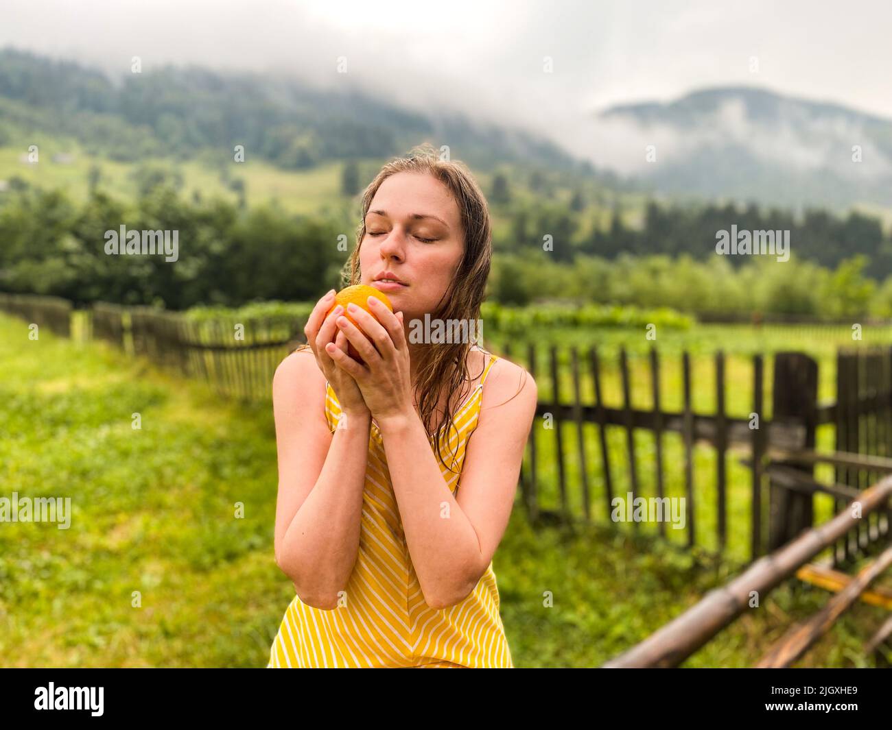 Eine schöne Frau, die eine Orange auf dem Hintergrund der Berge hält Stockfoto