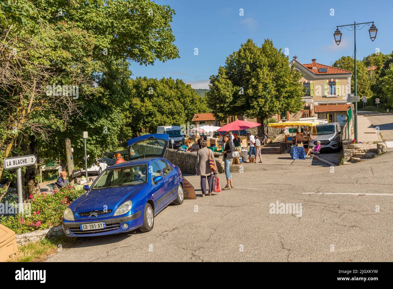 Farbenfrohe Marktzelte kennzeichnen mehrere Stände auf dem Dorfplatz von Plan-de-Baix in der Drôme, Frankreich. Kunden schlendern zwischen den Ständen. Ein Wegweiser nach La Blache steht am Straßenrand. Das Dorf mit 162 Einwohnern veranstaltet hier einen wöchentlichen Produzentenmarkt. Stockfoto
