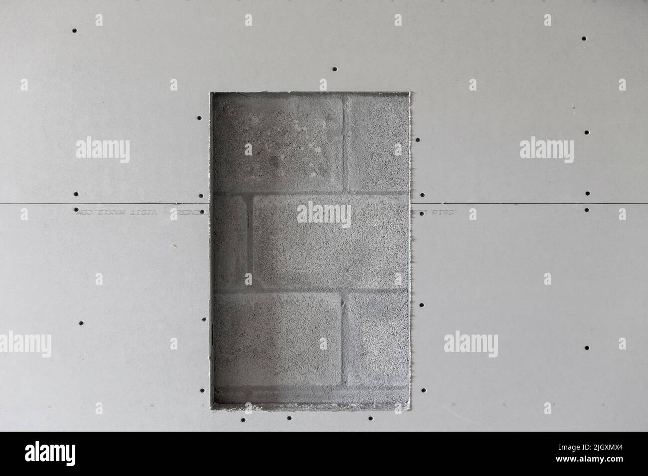 Trockenbauplatten, die auf Stahlstreben installiert sind, mit einer Öffnung für einen Feuerlöscher, die eine Betonblockwand freilegt. Stockfoto