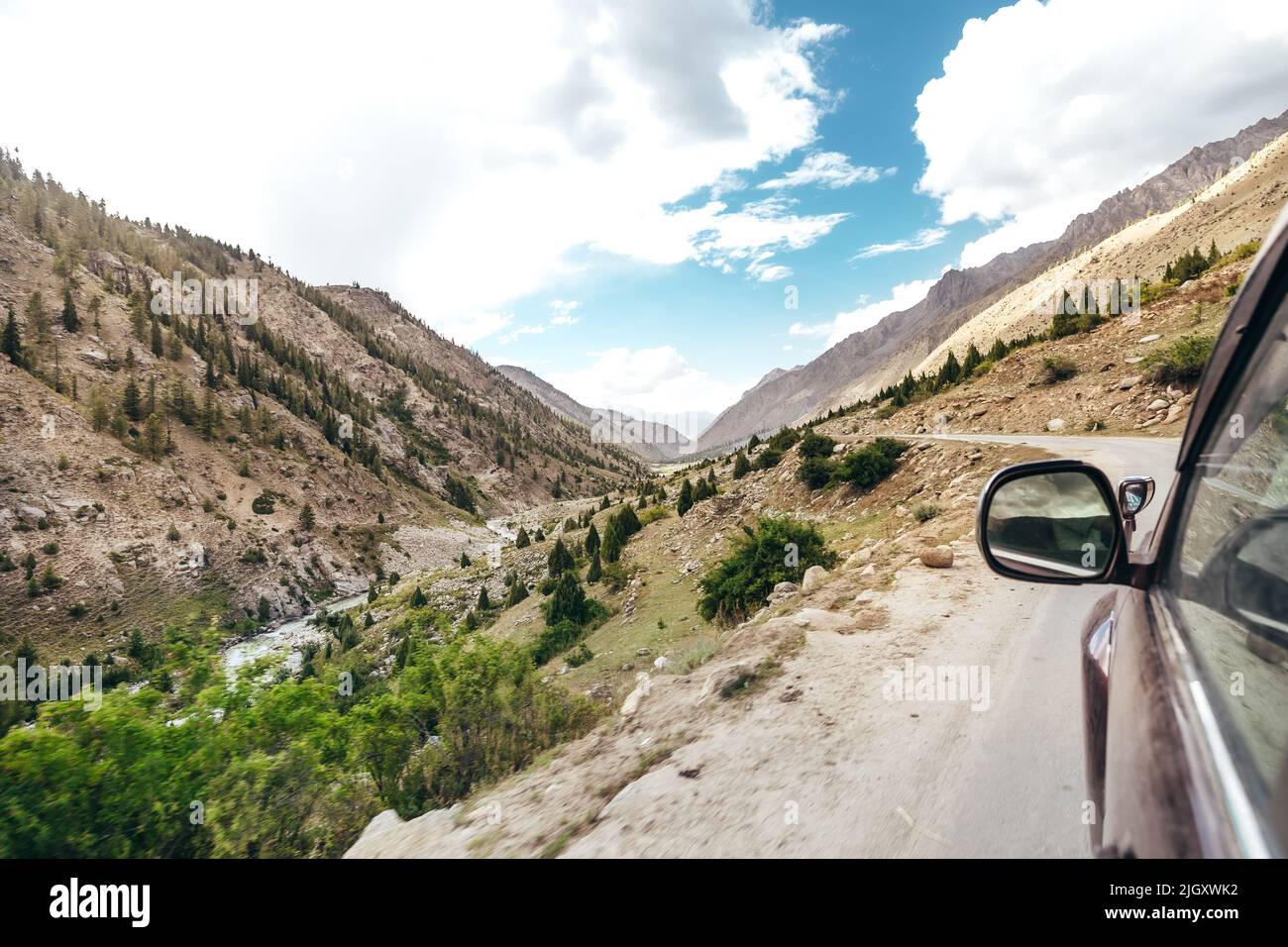 Rotes SUV-Auto, das am sonnigen Sommertag in Pakistan auf der Bergstraße durch den Flussschlucht des Astore Valley fährt Stockfoto