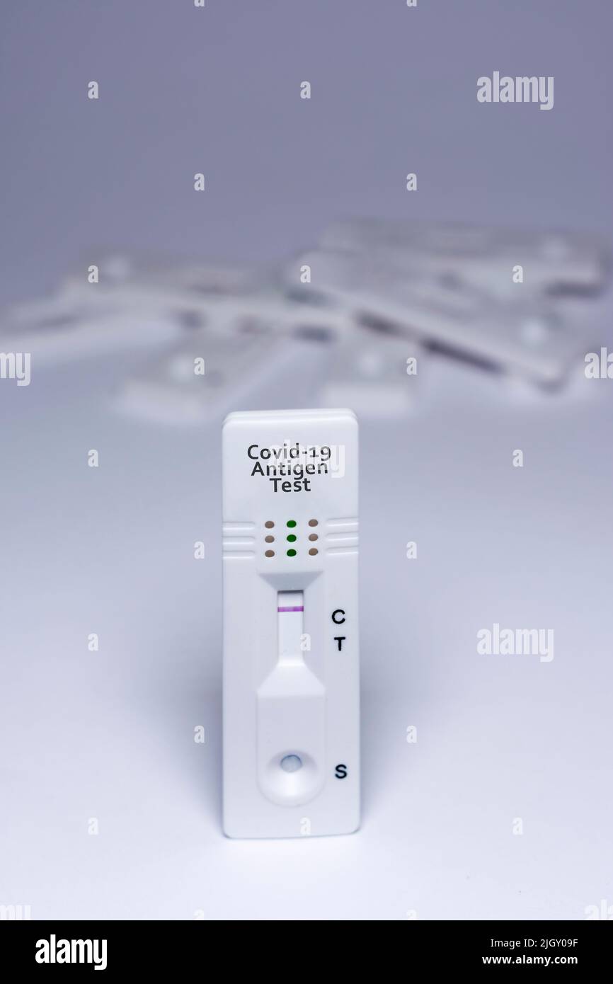 Ein Covid-19-Antigentest mit negativem Ergebnis, mit einem Stapel unfokussierter Tests im Hintergrund, auf weißem Hintergrund Stockfoto