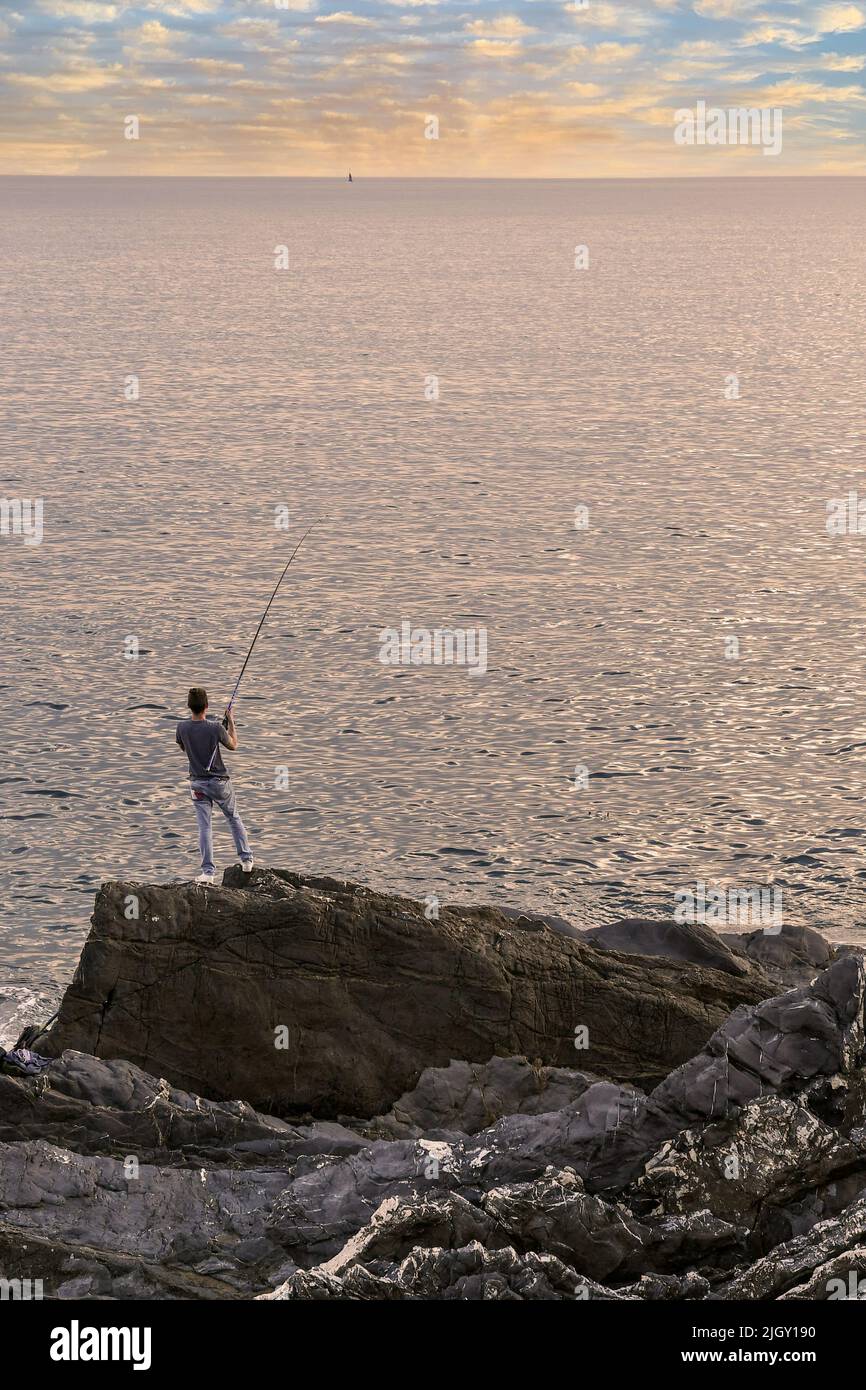 Ein Junge (14-15 Jahre alt) von hinten Angeln von der Klippe bei Sonnenuntergang, Nervi, Genua, Ligurien, Italien Stockfoto