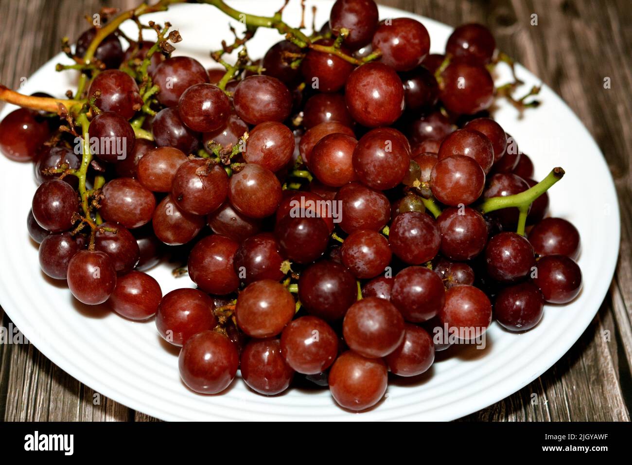 Haufen von frischen roten Trauben Früchte isoliert auf weißem Teller isoliert auf Holzhintergrund, selektive Fokus von einem Bund roter Trauben, gesunde frische Lebensmittel fru Stockfoto