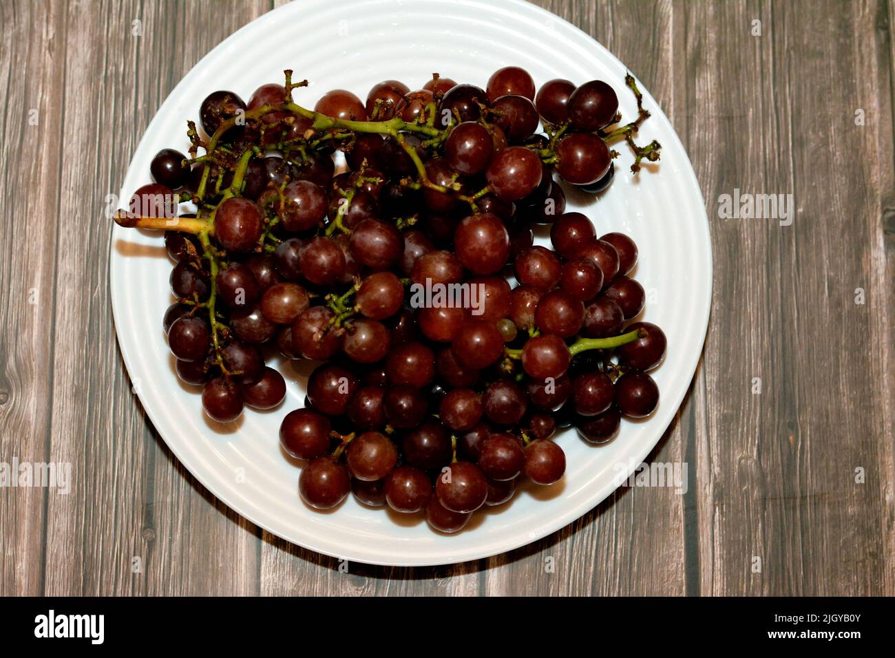 Haufen von frischen roten Trauben Früchte isoliert auf weißem Teller isoliert auf Holzhintergrund, selektive Fokus von einem Bund roter Trauben, gesunde frische Lebensmittel fru Stockfoto