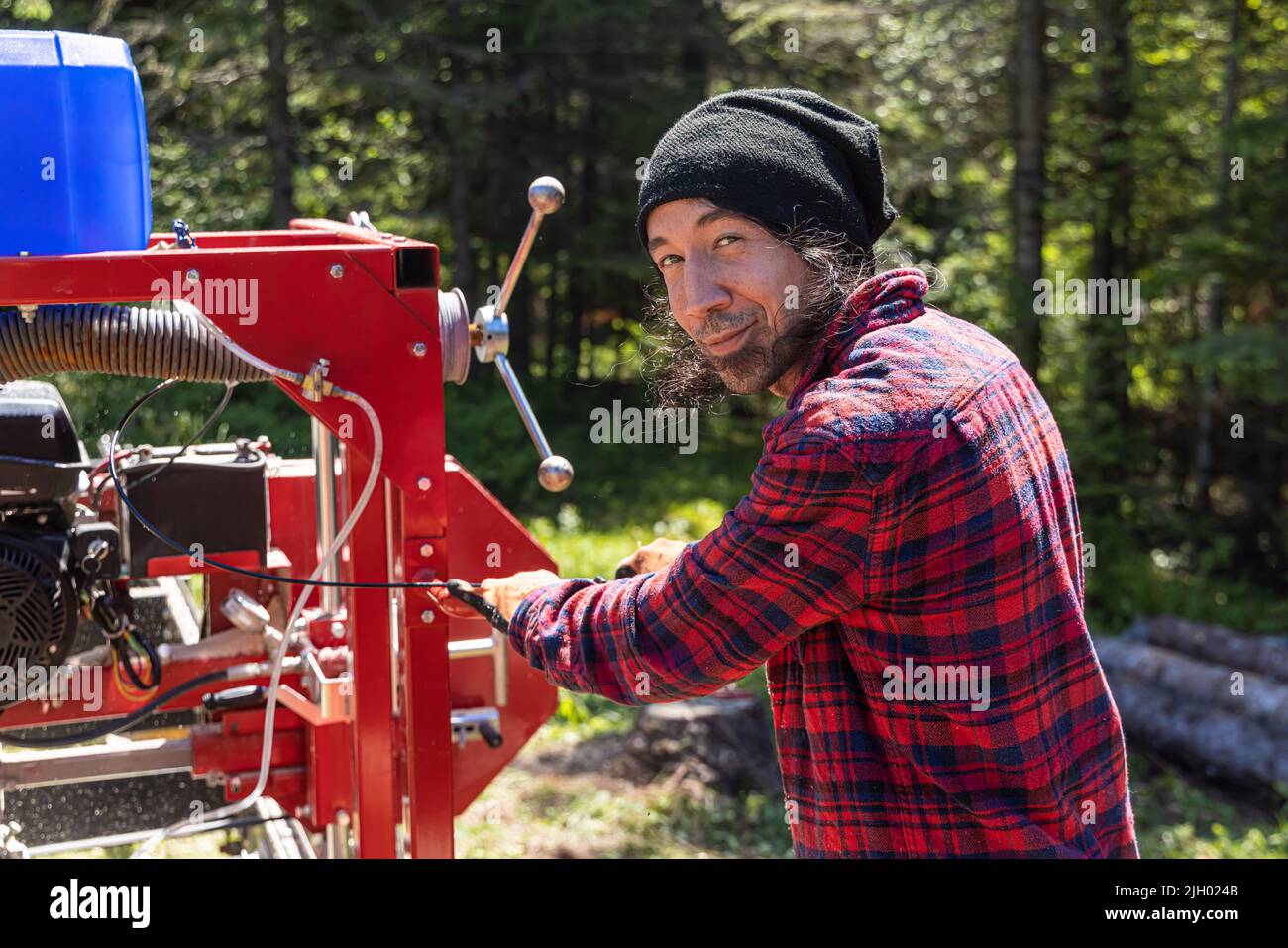 Porträt einer Sägemaschine, die bei der Arbeit mit schwarzen Haaren und Stoppeln in einem rot karierten Hemd arbeitet, mit einem mobilen Sägewagen mit Kopierraum. Stockfoto