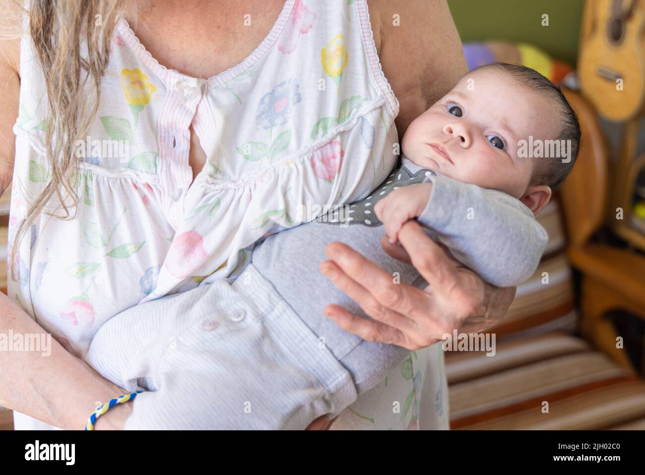 Nahaufnahme eines entzückenden, zwei Monate alten Mädchens, das einen grauen Pullover trägt, der in die Arme der Großmutter gewickelt ist und den Finger ergreifend. Mit Kopierbereich. Stockfoto