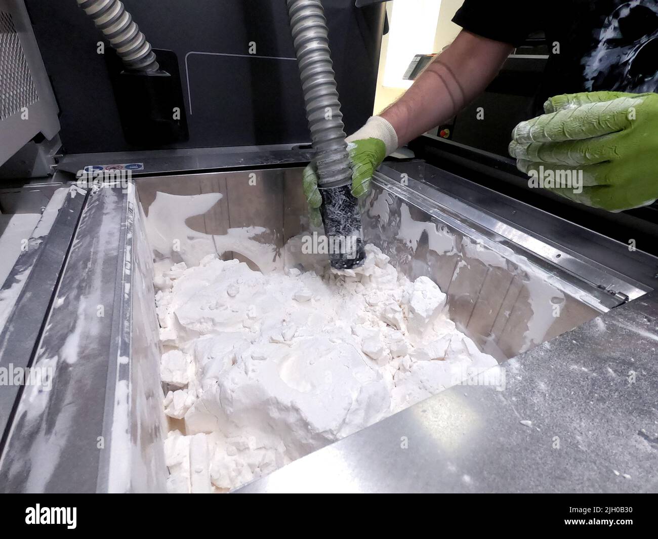 Ein Mann, der mit einem funktionierenden Staubsauger arbeitet, um das weiße  Pulver aus Polyamid von einem Modell zu reinigen, das auf einem 3D-Drucker  in einem 3D-Drucker gedruckt wurde. Reinigung von Objekten, die