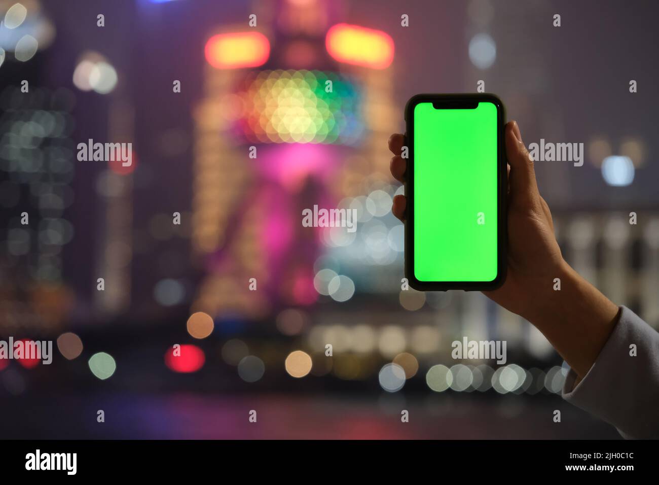 Hand zeigt grünen Bildschirm Telefon mit verwackelte bunte Shanghai Stadt Bokeh Hintergrund Stockfoto