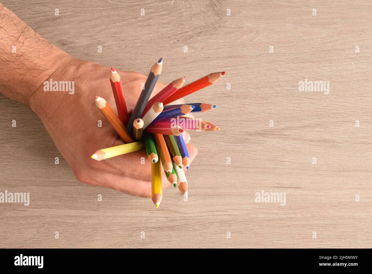 Hand eines Mannes, der eine Gruppe von Buntstiften auf einem Holztisch hält. Draufsicht Stockfoto