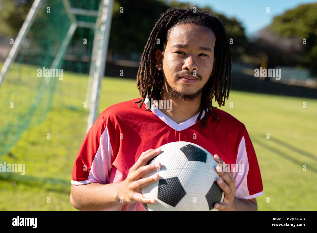 Porträt eines selbstbewussten männlichen Birazialspielers mit Dreadlocks in rotem Jersey und Ballhaltung Stockfoto