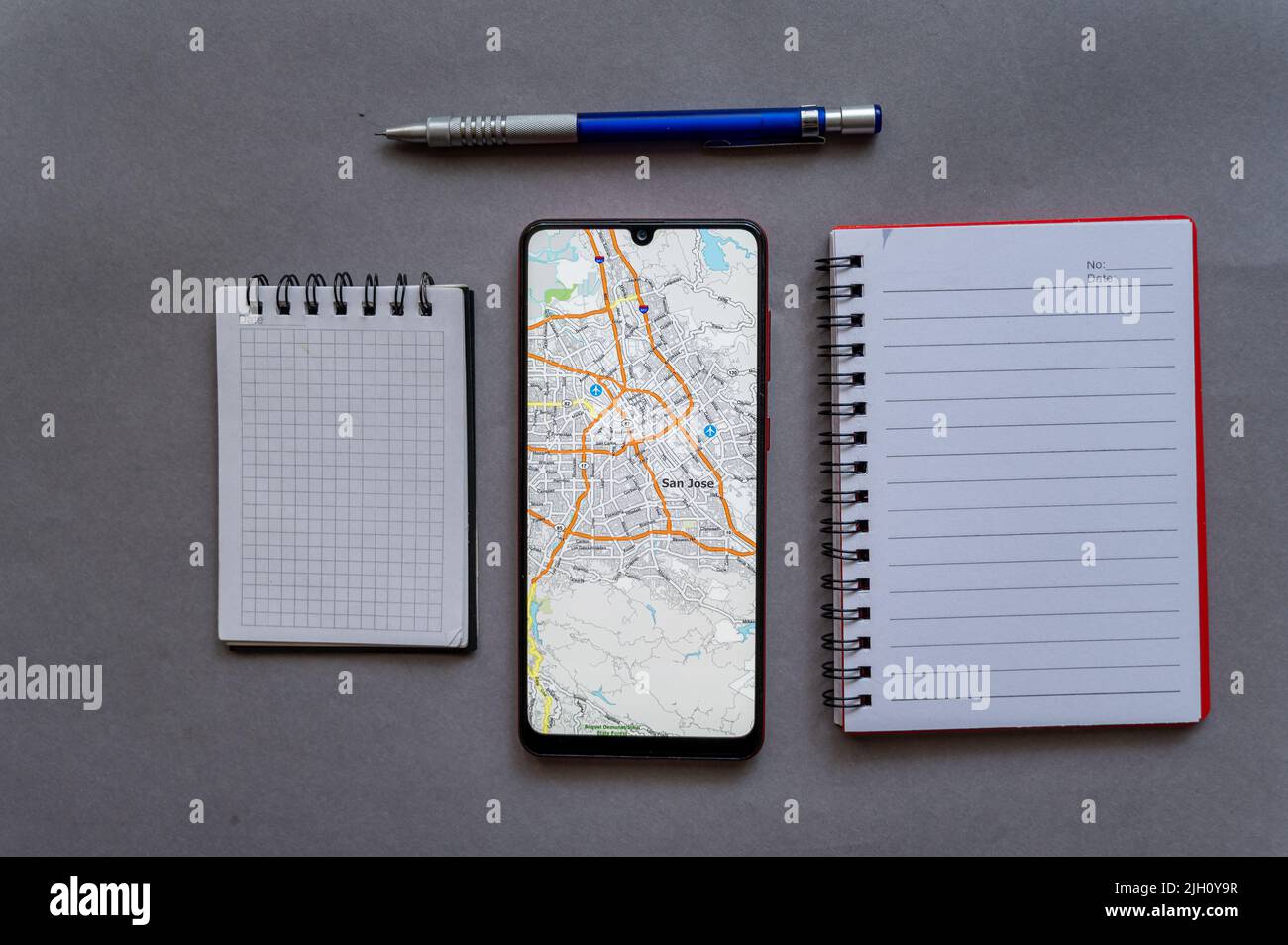 Smartphone und zwei offene Notebooks auf grauem Hintergrund. Karte der Stadt San Jose auf dem Bildschirm des Geräts. San Jose ist die Hauptstadt des Silicon Valley, Stockfoto